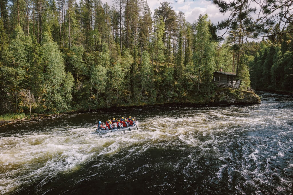 Rafting through the rapids of the Kitka River in Kuusamo on a sunny summer day, surrounded by pristine northern wilderness and lush forests.
