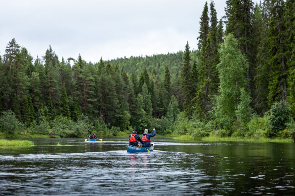 Adventure camp participants paddling on the Oulanka River, surrounded by rugged cliffs and northern wilderness.